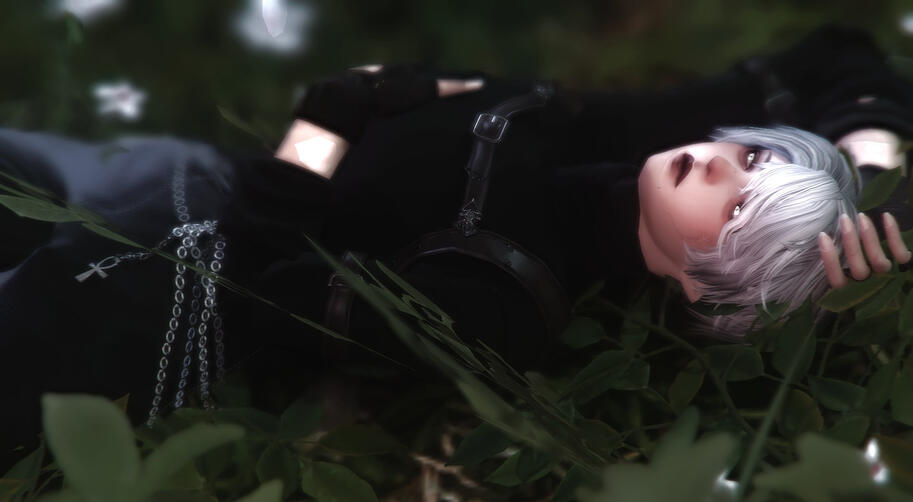 A man laying in a field of twisting, overgrown grass and little flower blooms. He has one arm folded over his belly while the other is placed above his head, and his eyes flit to the side, lids lowered and lips in a faint perpetual frown. Despite his appea